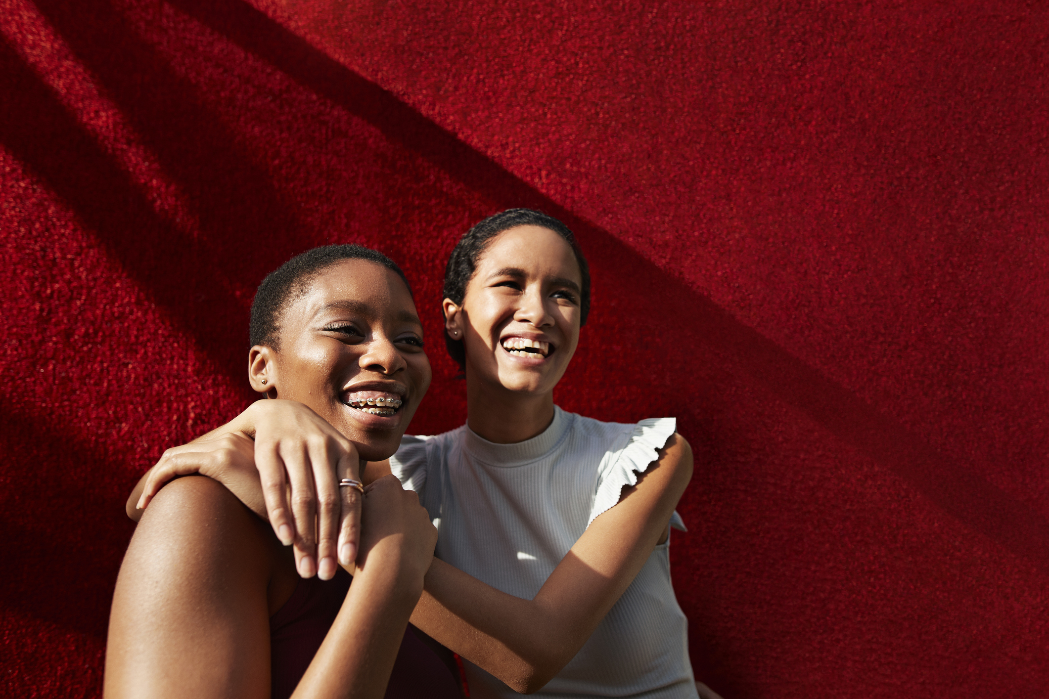 Smiling young woman standing with female friend against red wall.