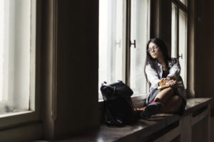 Young woman student looking through window and holding in hands notebooks