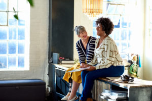 Two female friends sitting on sideboard and smiling, friendship, fun, memories, wellbeing