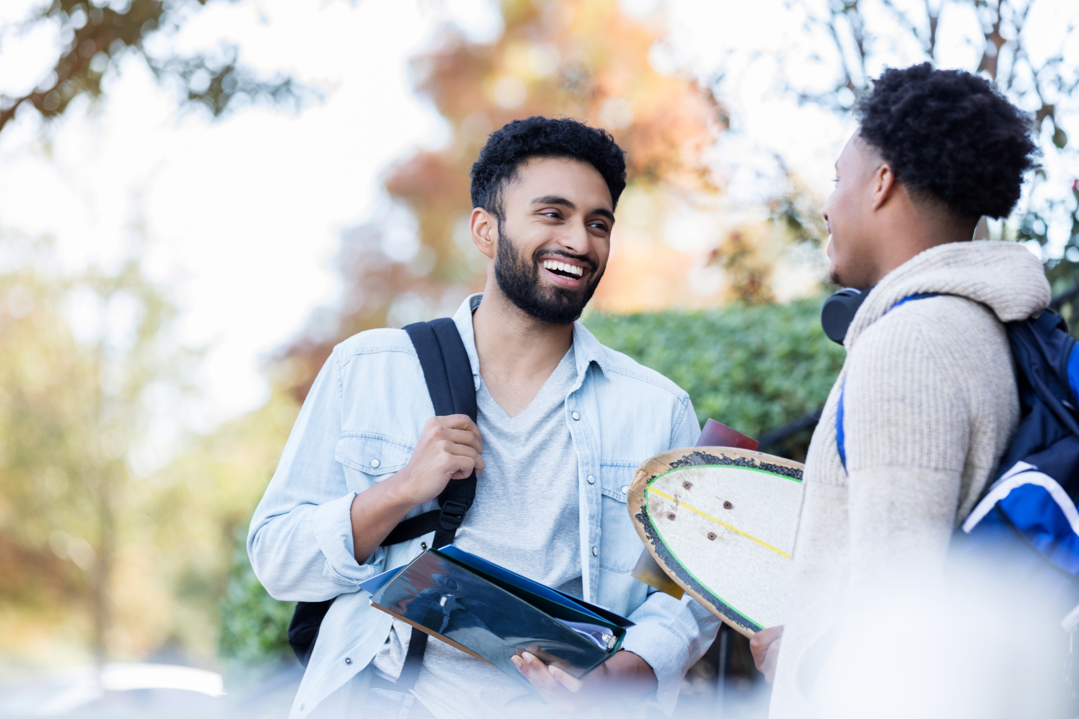 Two young male college students stand together outdoors on their college campus and enjoy a discussion.