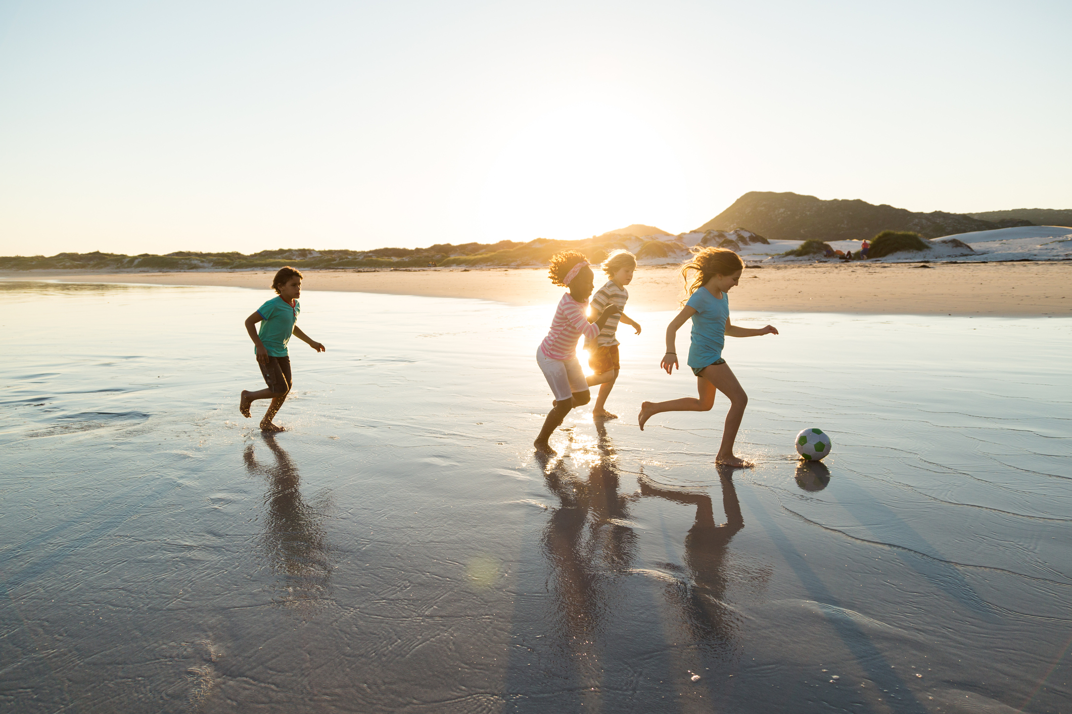 Group of children playing soccer together on a beach at sunset