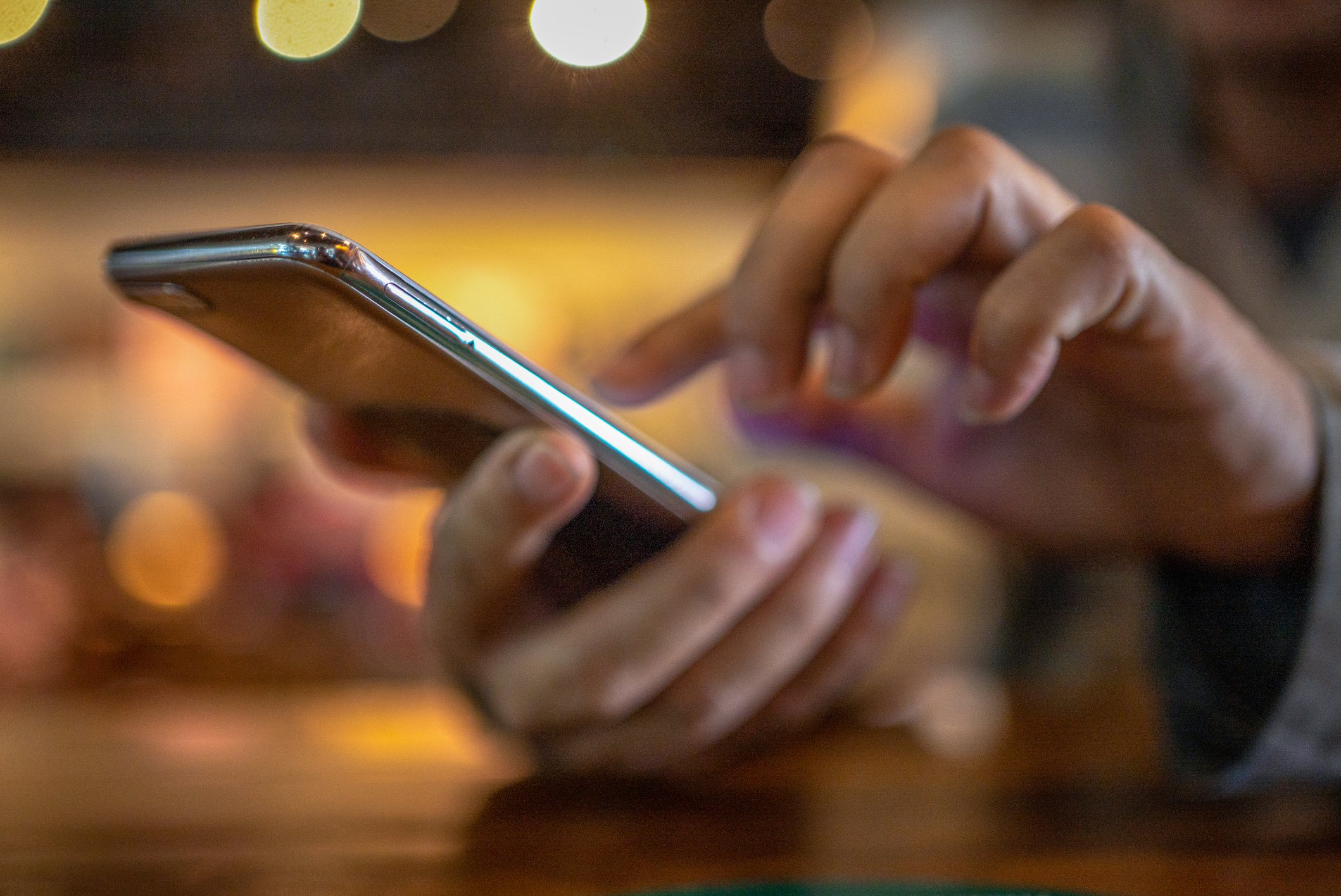 Closeup image of a man holding and using smart phone with coffee cup on wooden table in cafe.