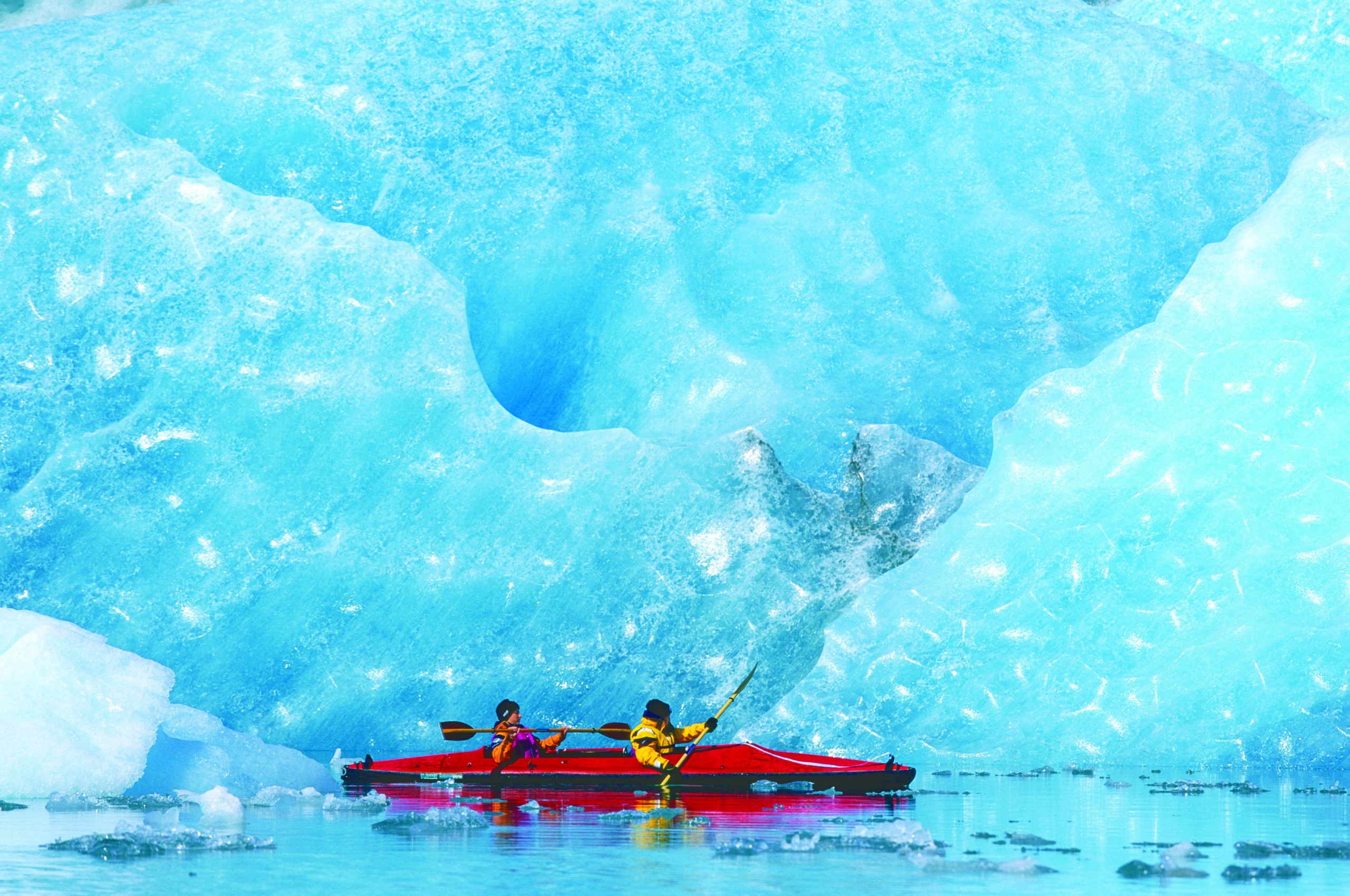 A pair of sea kayakers paddle along Bear Glacier in Kenai Peninsula, located in Kenai Fjords National Park, Alaska.